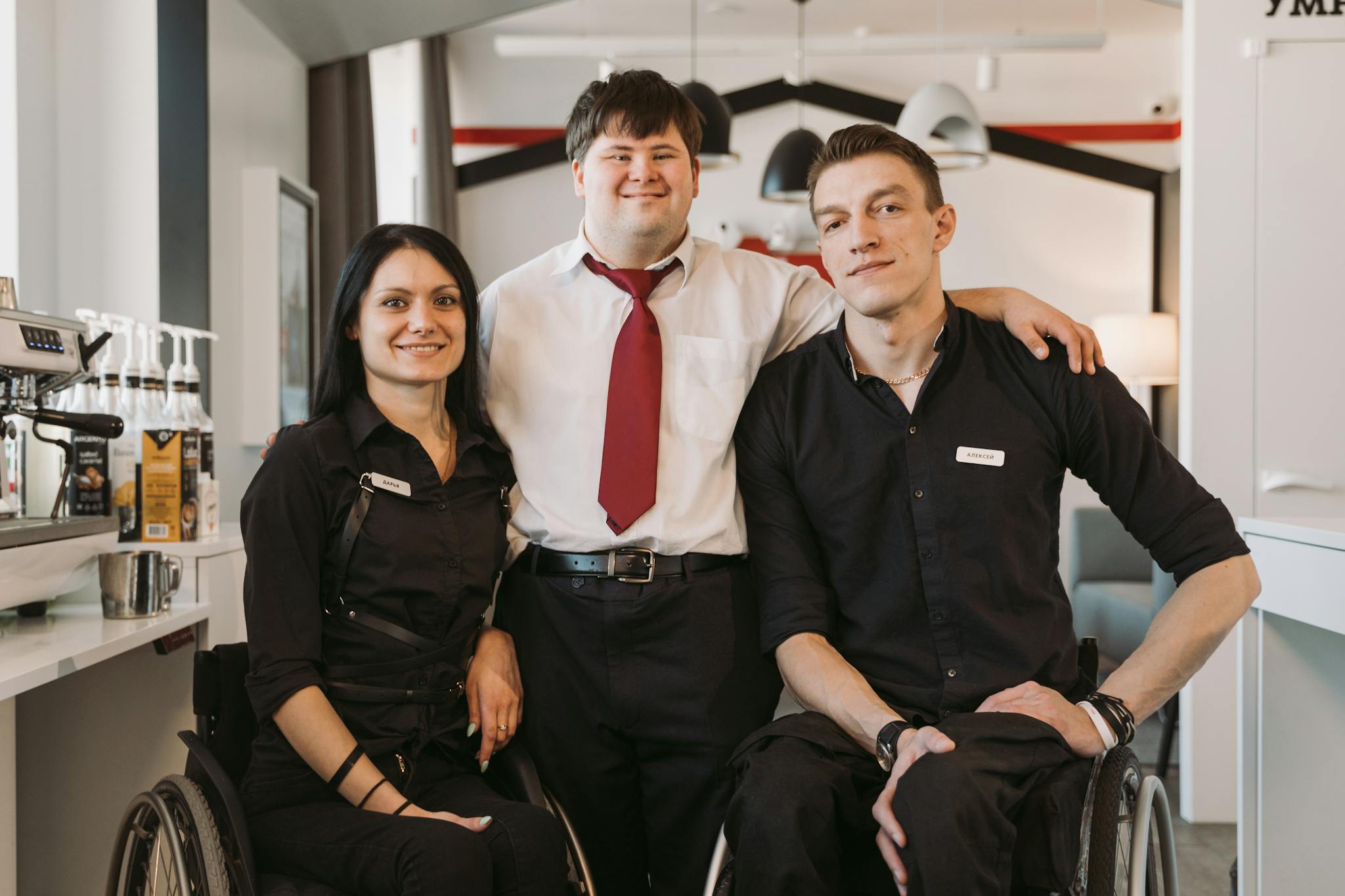 A group of diverse adults, including those in wheelchairs, smiling in a cafe environment fostering teamwork.