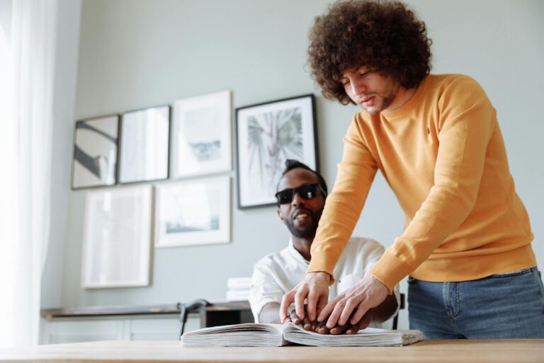 Two men engaged in Braille reading, promoting assistive technology and independence.
